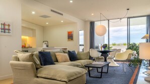 A modern living room with a sectional sofa, a dining area, and a large window offering a view. - Executive Rental - Campbelltown (Campbelltown)