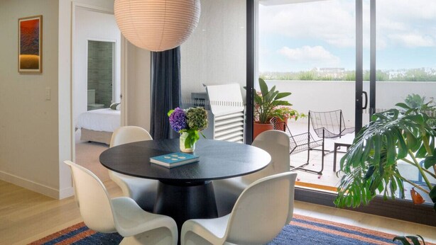 A modern living room with a round black table, white chairs, a hanging light fixture, and a view of the outdoors through large sliding doors. - Executive Rental - Campbelltown (Campbelltown)