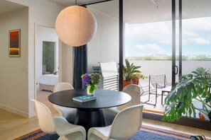 A modern living room with a round black table, white chairs, a hanging light fixture, and a view of the outdoors through large sliding doors. - Executive Rental - Campbelltown (Campbelltown)