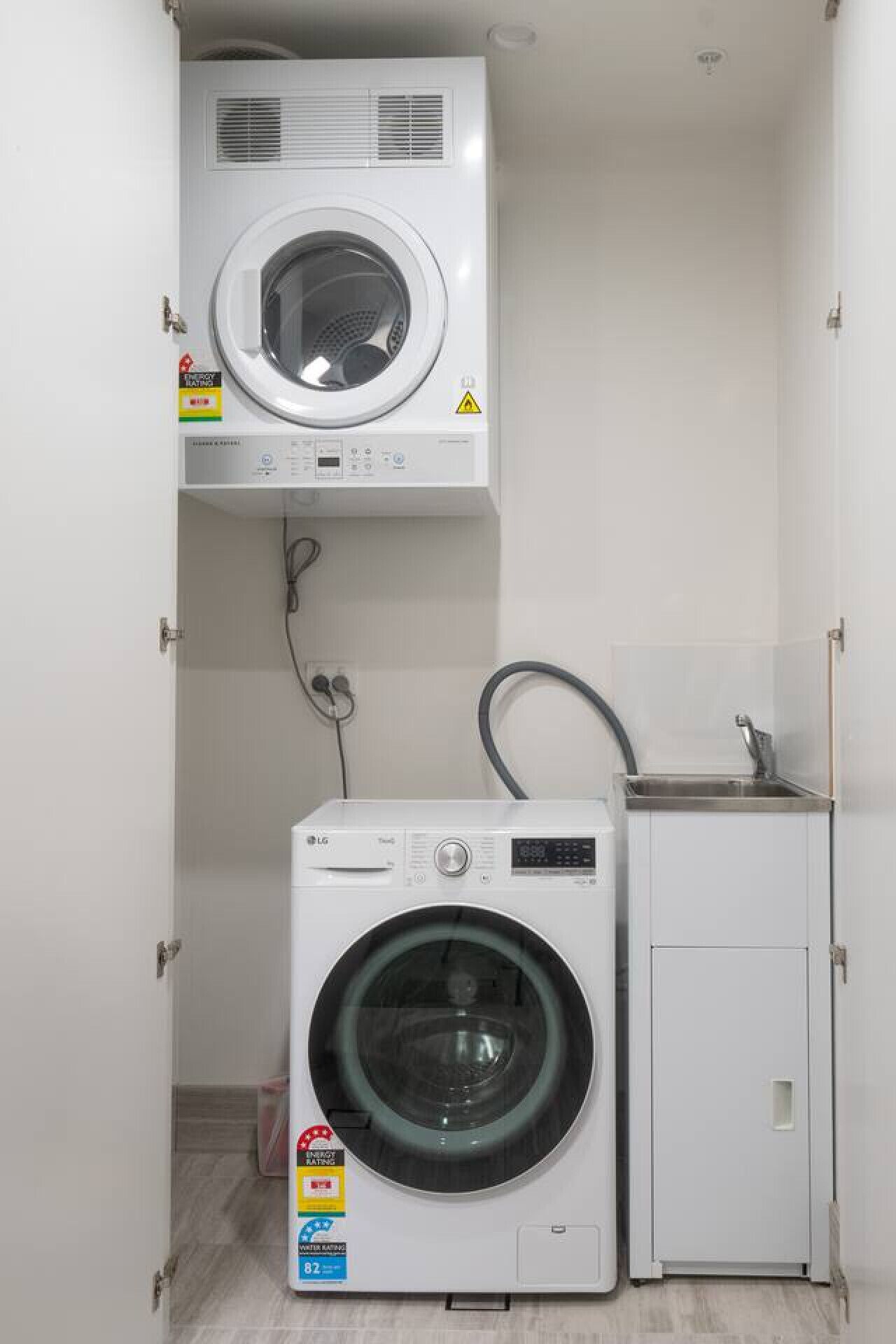 A compact laundry room with a front-loading washing machine and a top-loading dryer, both white, with a small sink and cabinet.