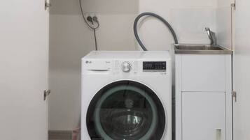 A compact laundry room with a front-loading washing machine and a top-loading dryer, both white, with a small sink and cabinet.