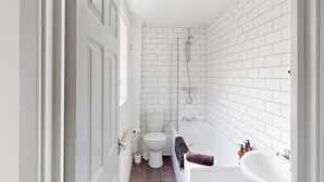 Et badeværelse med hvide fliservægge, toilet, bruser og badekar.