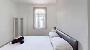 Et soveværelse med seng, garderobeskab, et vindue og et lille natbord med en plante.