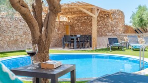 Un espace aménagé au bord de la piscine, avec un mur en pierre, des sièges d’extérieur et une pergola.