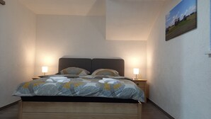 Una cama con cabecera, lámparas de noche e imagen colgada en la pared.