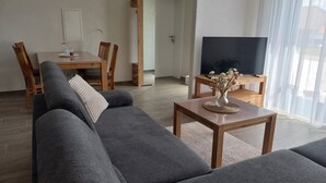 Una sala de estar moderna con un sofá gris, una mesa de comedor de madera y un televisor sobre un mueble.