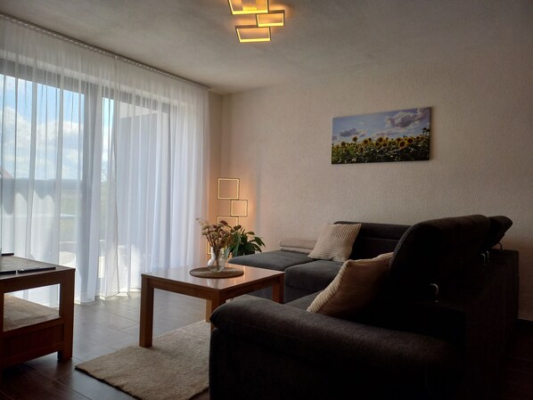 Ein Wohnzimmer mit einer Couch, einem Couchtisch, einem Gemälde und einem Fenster mit durchsichtigen Vorhängen.