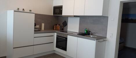 A modern kitchen with white cabinets, a built-in oven, a microwave, and a sink.
