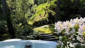 A hot tub surrounded by lush greenery and flowering plants. - Private Cabin w/ Hot Tub • Near Beaches & Trails 30 min from Victoria • King Bed (Victoria)