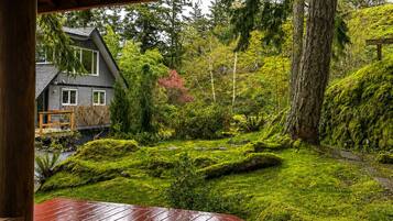 A wooden deck with a bench, overlooking a lush garden with a house in the background.