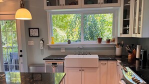 A modern kitchen with white cabinets, a black countertop, and a window overlooking greenery. - Private Cabin w/ Hot Tub • Near Beaches & Trails 30 min from Victoria • King Bed (Victoria)