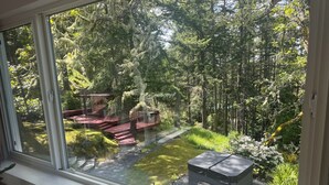 A view through a window of a forested area with a wooden deck and a small shed. - Private Cabin w/ Hot Tub • Near Beaches & Trails 30 min from Victoria • King Bed (Victoria)