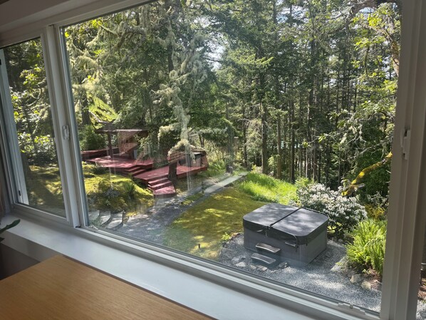 A view through a window of a forested area with a wooden deck and a small shed.