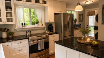 A modern kitchen with white cabinetry, stainless steel appliances, and a black countertop.