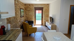 A compact living space with a stone wall, a sofa, a dining table, and a TV.