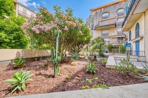A courtyard with a variety of plants, including a cactus and flowering shrubs, surrounded by multi-story buildings with balconies.