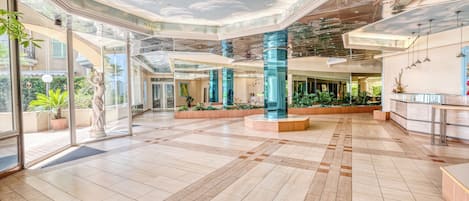 A spacious lobby with a high ceiling, large glass doors, and a central seating area with blue pillars.