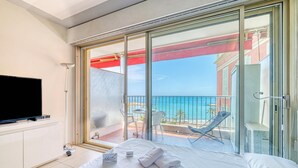 Ein Hotelzimmer mit Bett, Fernseher, einem Balkon mit Stuhl und Blick aufs Meer.