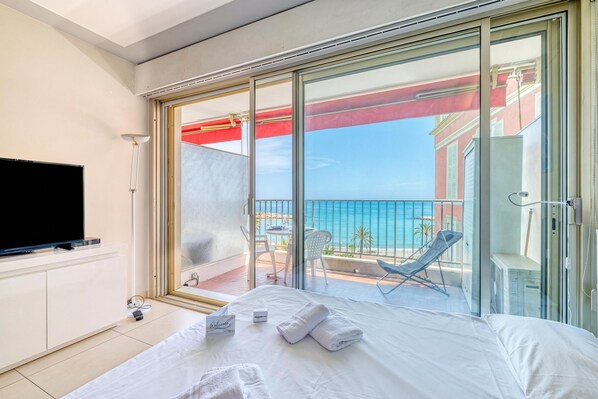 A hotel room with a bed, a TV, a balcony with a chair, and a view of the sea. - Garavan Studio 13 with Sea View Terrace, Menton, France (Menton)