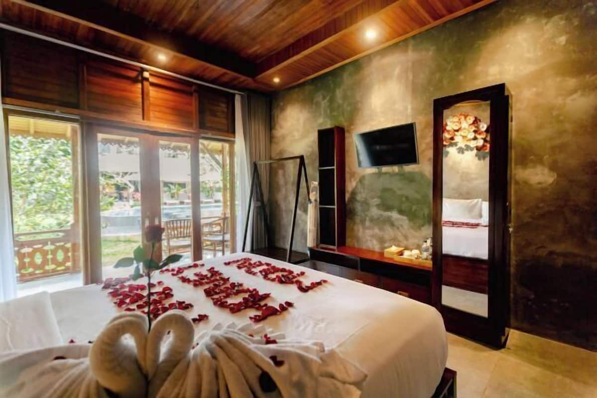 A hotel room with a bed, a TV, a mirror, and a view of the outdoors.