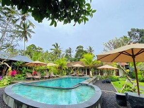 A pool area with lounge chairs and umbrellas, surrounded by tropical vegetation and palm trees. - Puri Kurnia Ayu (Payangan)