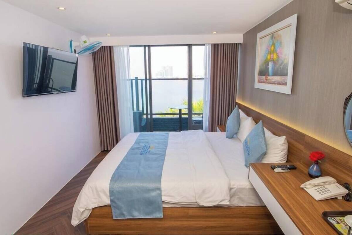 A hotel room with a bed, a TV, a desk with a phone, and a window with a view of a building.