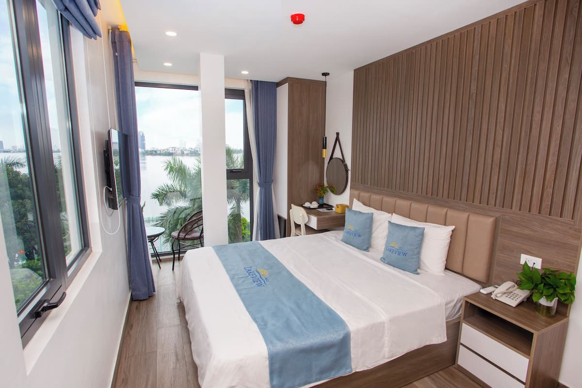A modern hotel room with a large bed, a desk, and a view of a cityscape.