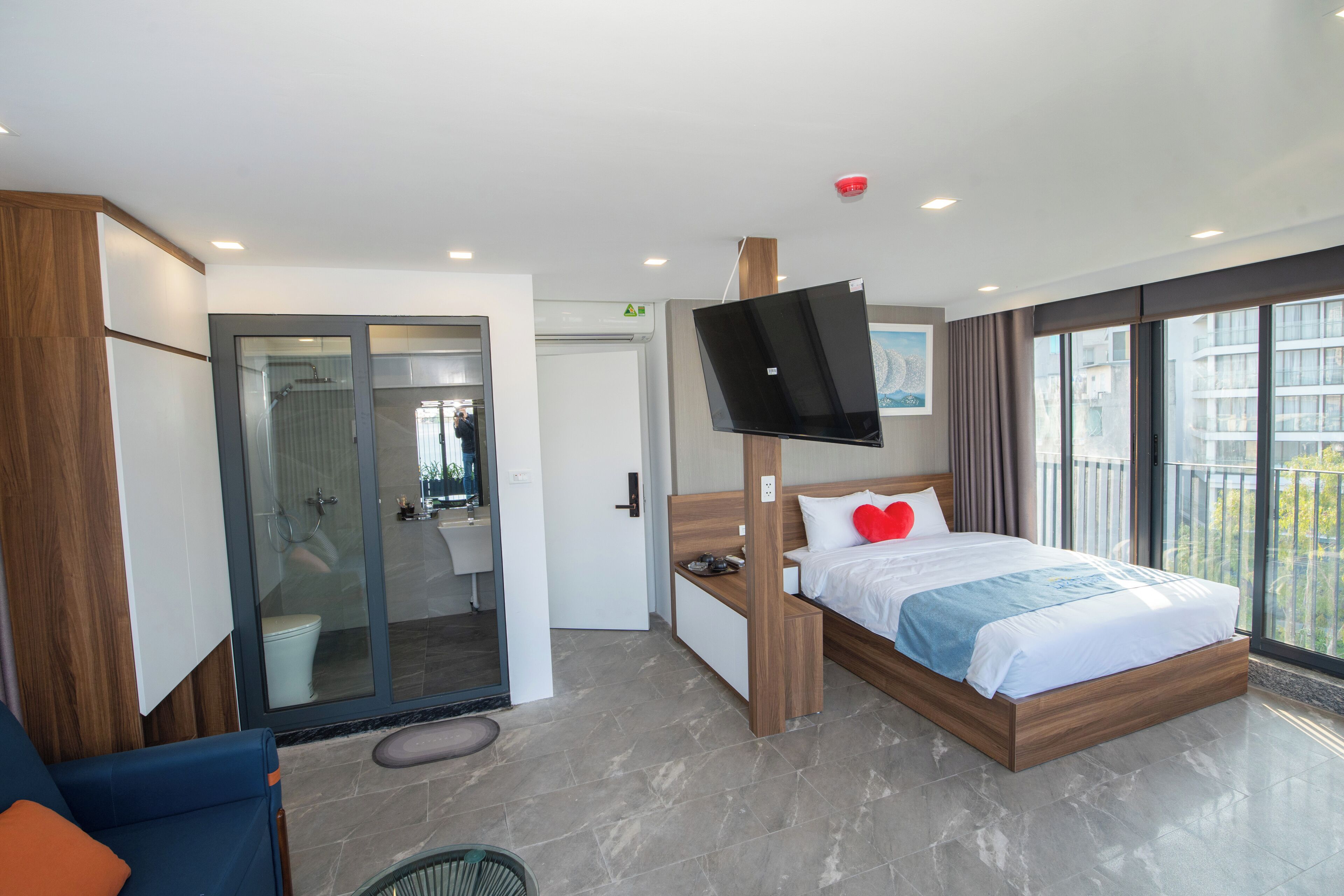 Una habitación de hotel moderna con una cama, televisor, escritorio y baño con puerta de vidrio.