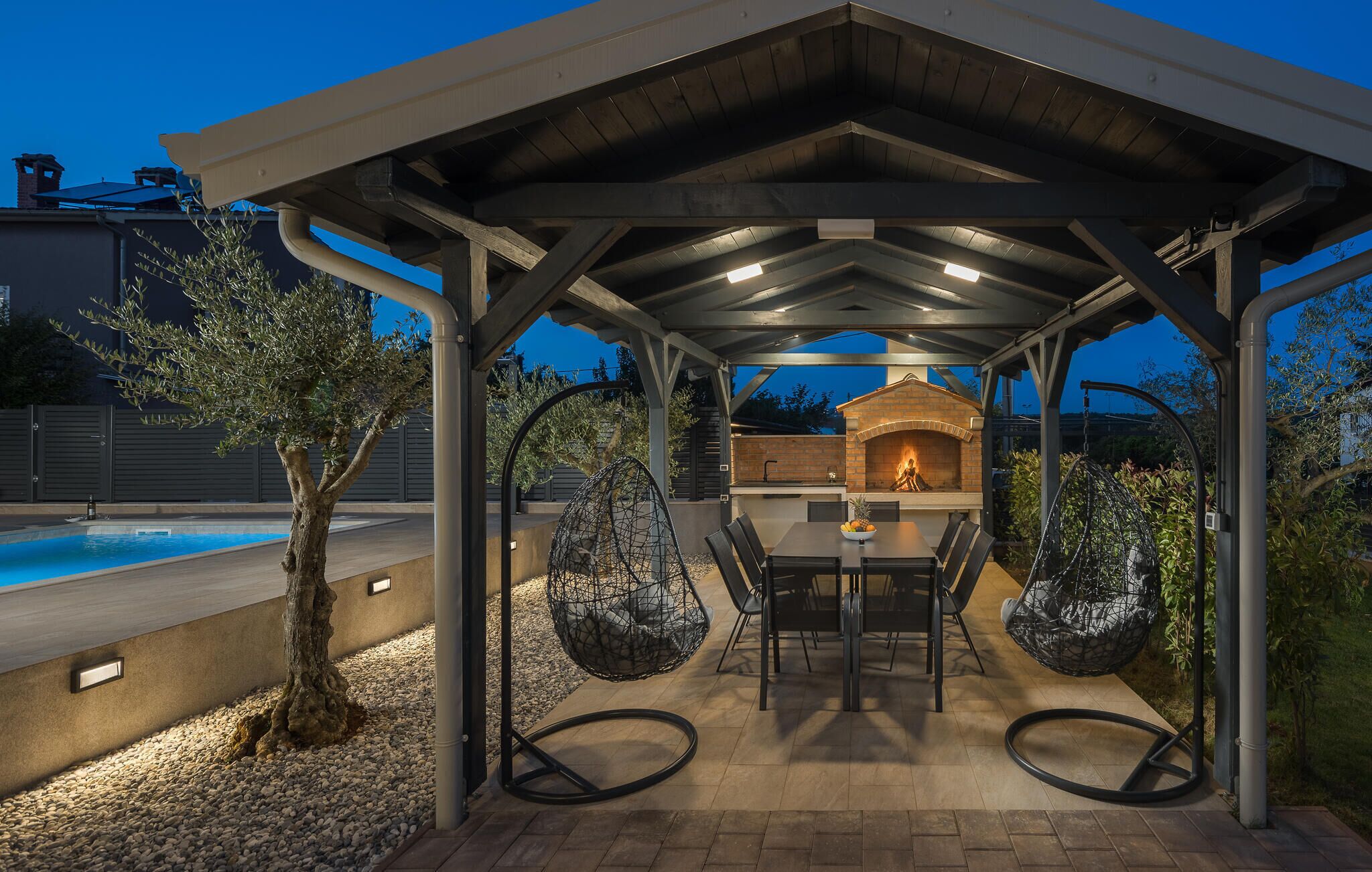 Eine Terrasse im Freien mit einem Backofen aus Ziegeln, Sitzgelegenheiten und einem Pool.