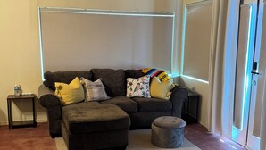 A living room with a sectional sofa, ottoman, and a ceiling fan. - Rustic, Artsy Studio w/ Desert Panoramic Views  (Black Canyon City)
