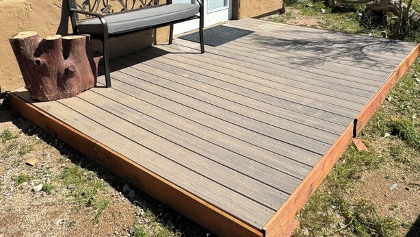 A wooden deck with a bench and a tree stump, a building with a sliding glass door, and a clear view of the surrounding landscape. - Rustic, Artsy Studio w/ Desert Panoramic Views  (Black Canyon City)