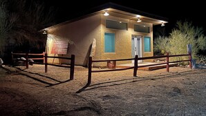 A small, single-story building with a flat roof, a wooden fence, and a dirt ground. - Rustic, Artsy Studio w/ Desert Panoramic Views  (Black Canyon City)