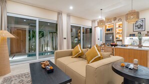 A modern living room with a sofa, a coffee table, and a kitchen area visible through glass doors. - Villa Palima (Canggu)