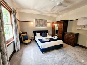 Een slaapkamer met een groot bed, een stoel, een garderobe en een plafondventilator.