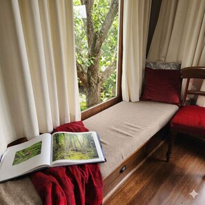 Ein Zimmer mit einem Bett, einem Vorhangfenster, einem Sessel und einem Buch.