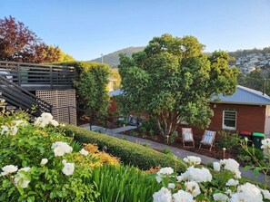 A landscaped garden with a variety of plants and flowers, a wooden deck, and a building with a red brick facade.