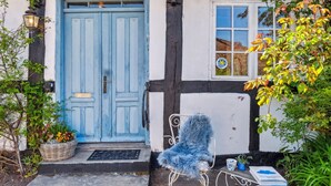 Ein traditionelles Gebäude mit einer blauen Tür, einem weißen Fenster und einer kleinen Veranda mit Stuhl und Tisch.
