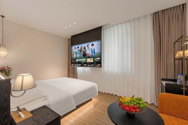 A hotel room with a bed, a television, a coffee table with fruit, and a sofa.