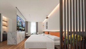 Moderni hotellihuone, jossa on suuri sänky, marmorilla koristeltu seinä, televisio ja puulattia.