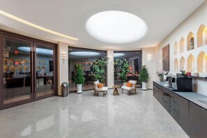 A hotel lobby with a central seating area, a reception desk, and a large circular skylight.