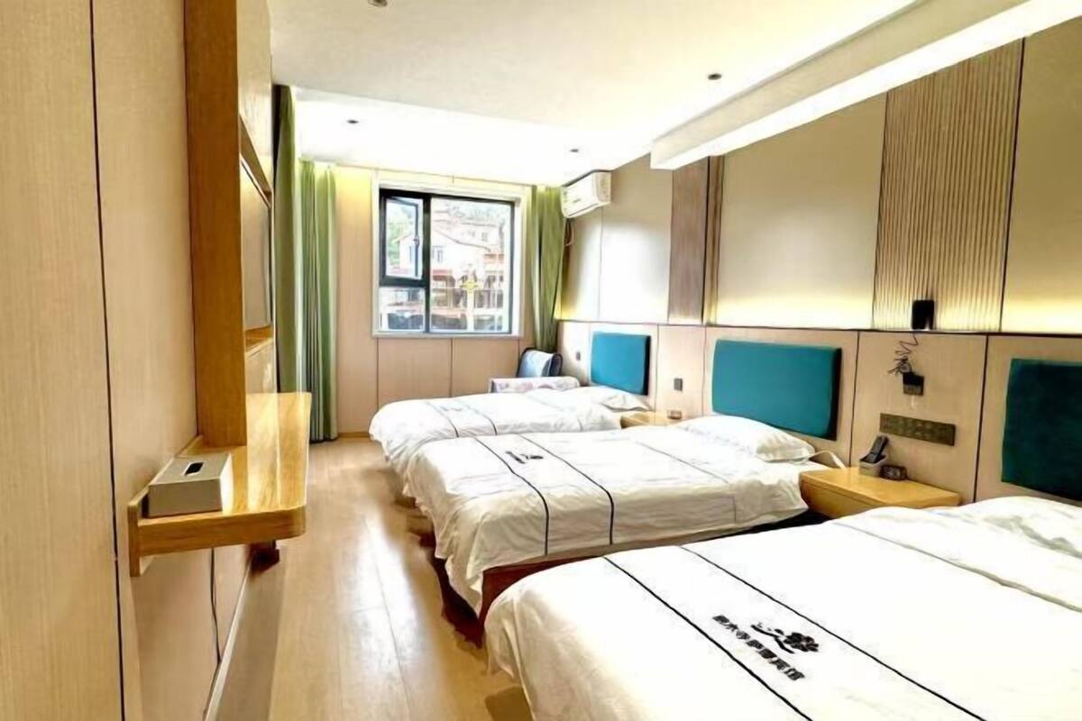 Habitación de hotel con dos camas, una ventana con cortinas, una mesita de noche con lámpara y un equipo de aire acondicionado instalado en la pared.