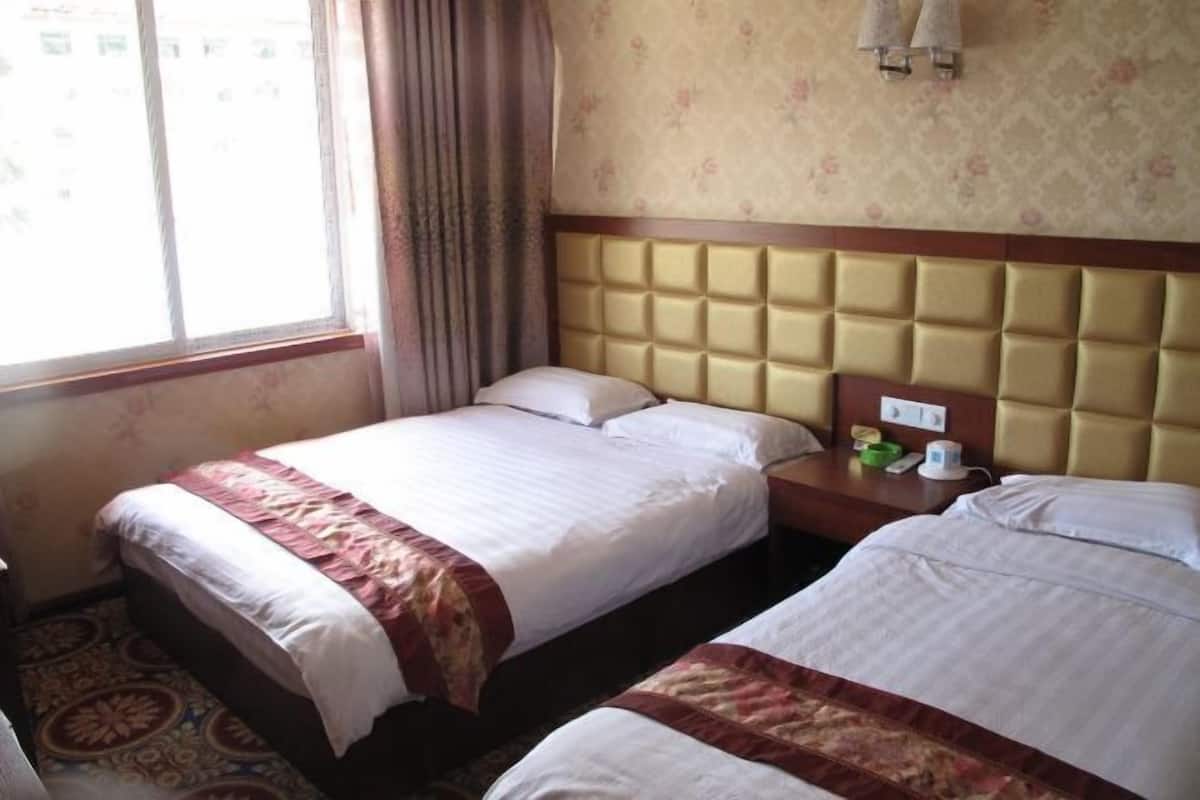 A hotel room with two beds, a headboard, a nightstand, a window with curtains, and a patterned carpet.