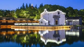 A traditional building with a reflection in a calm body of water, surrounded by trees and a clear sky.