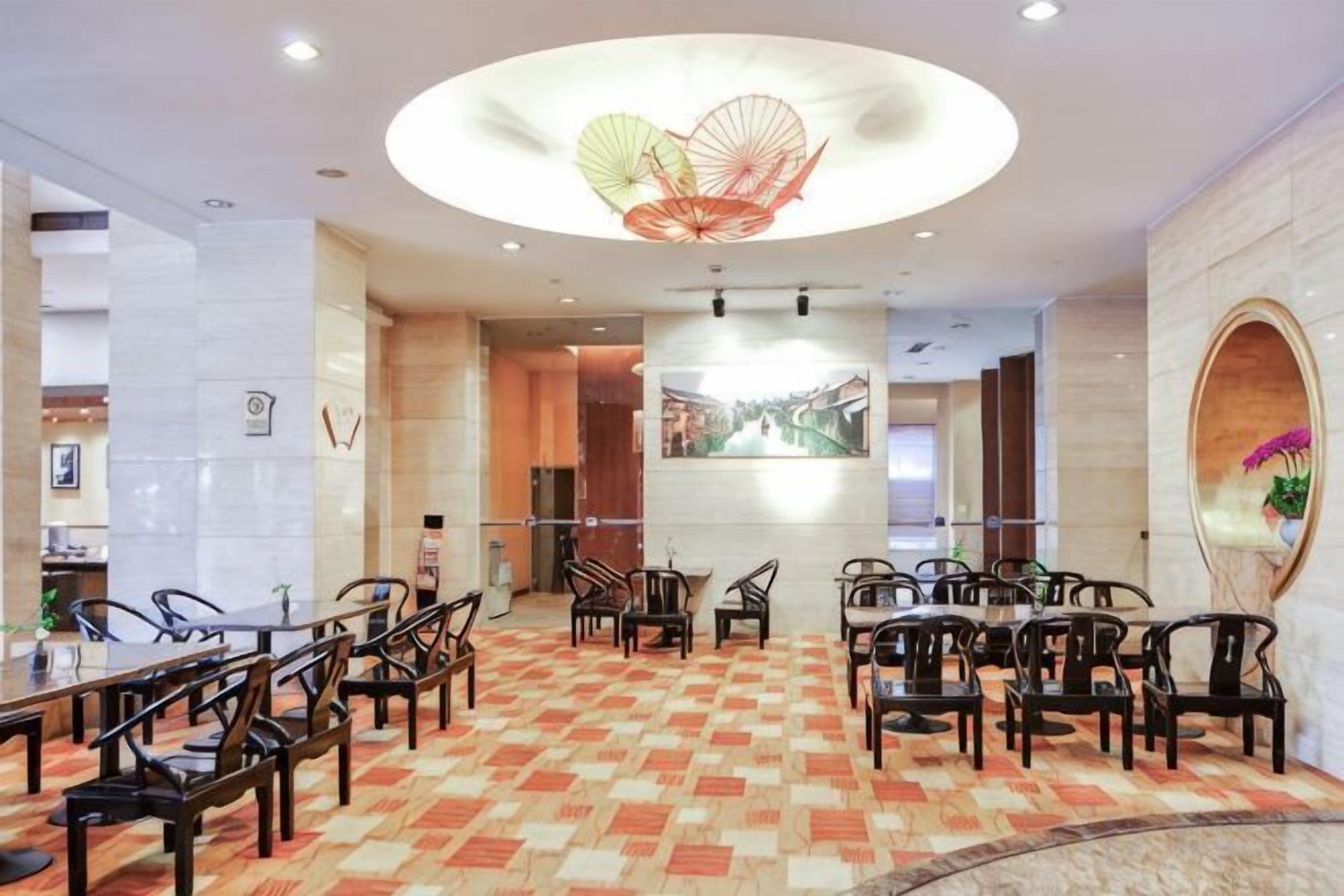 A hotel dining area with round tables and chairs, a patterned carpet, and a large circular light fixture.
