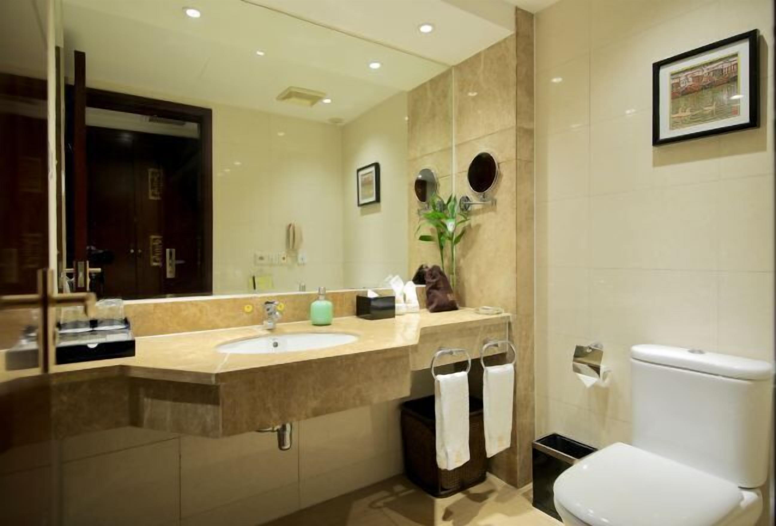 A modern bathroom with a large mirror, a sink, a toilet, and a trash bin.