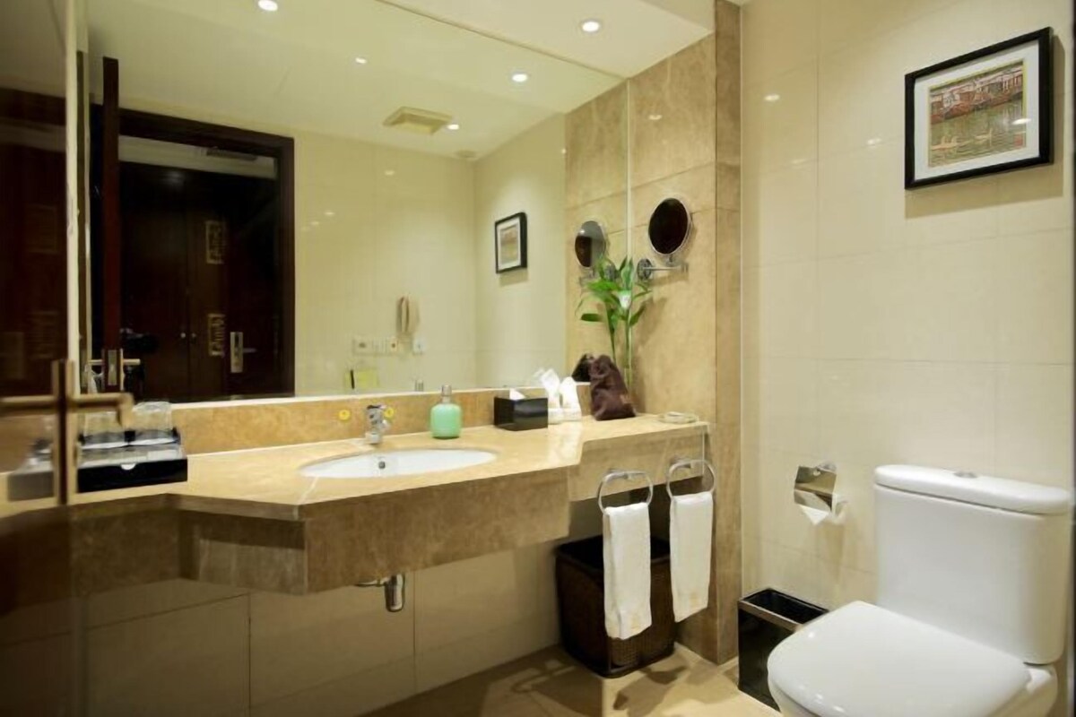 A modern bathroom with a large mirror, a sink, a toilet, and a trash bin.