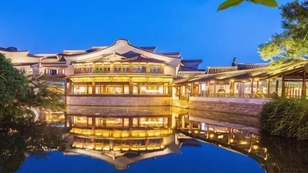 Un edificio tradicional de varios niveles, con su reflejo en el agua, y un cielo despejado.