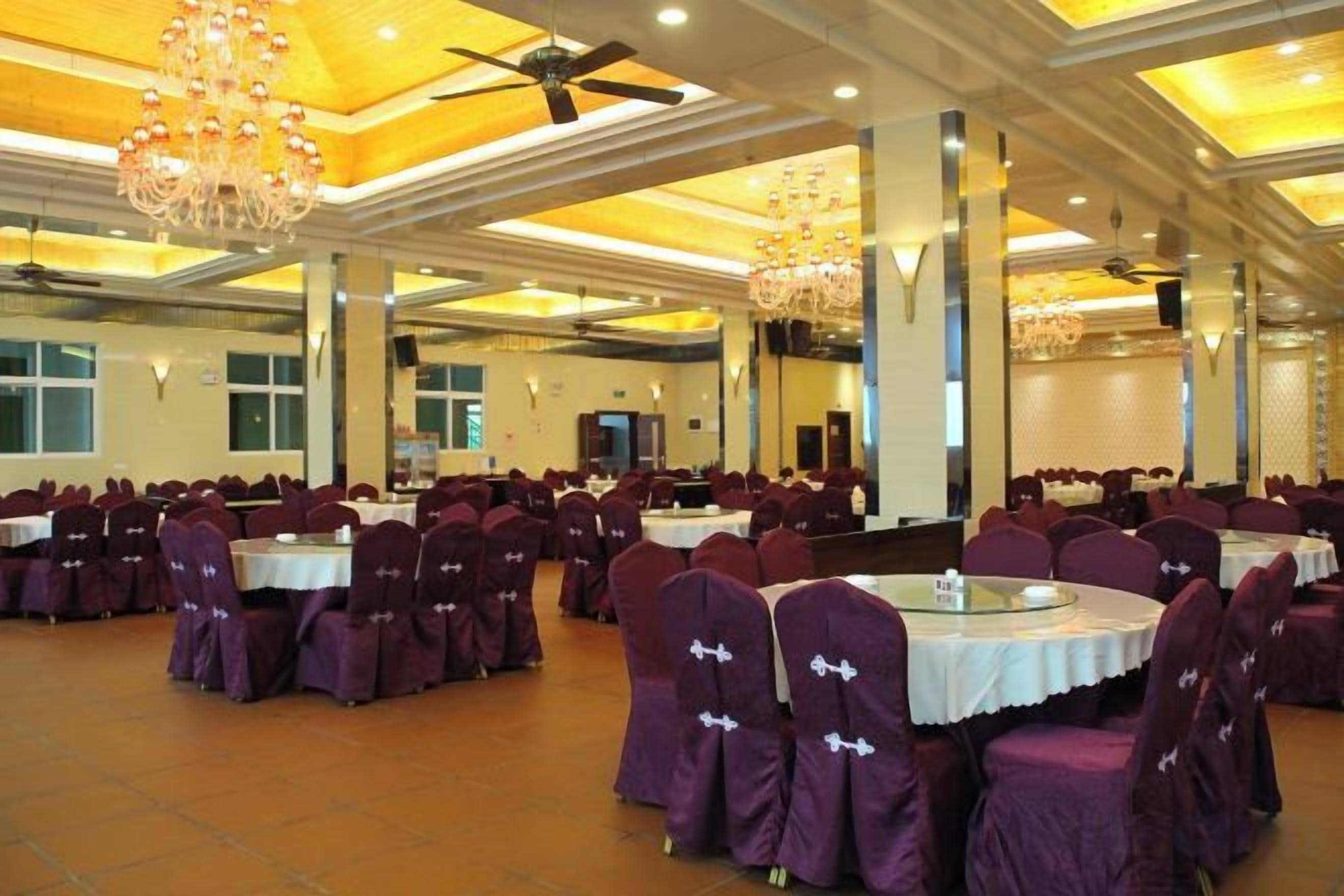 Un salón de banquetes con mesas redondas y sillas, un ventilador de techo y candelabros.