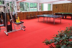 Une pièce dotée d’une moquette rouge, d’appareils de musculation, d’une table de ping-pong et d’une table de billard.