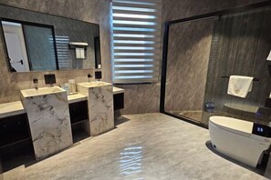 Un baño moderno con encimeras de mármol, un espejo grande, un inodoro y una cabina de ducha con mampara de vidrio.